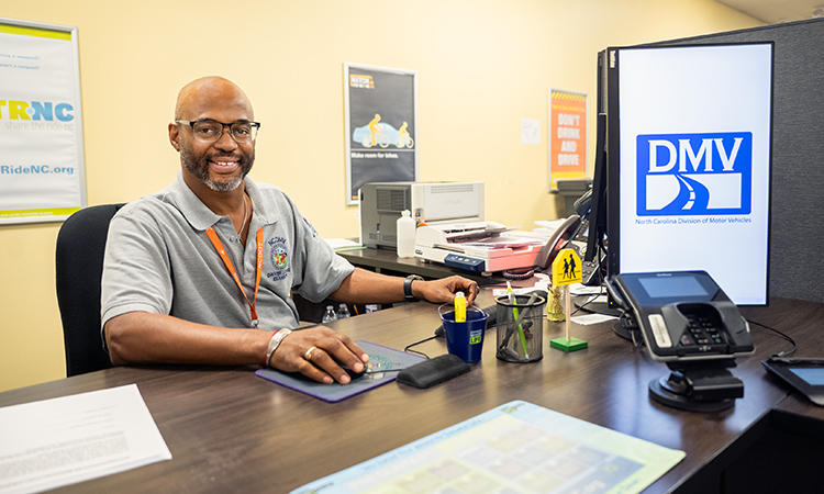 An NCDMV examiner sits at his desk smiling for the camera