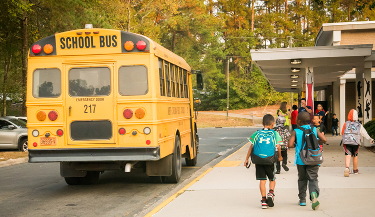 Students walking past a school bus at school.