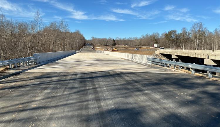 A newly constructed bridge stretches across a landscape with trees on either side.
