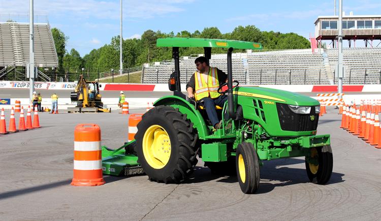 A man drives a tractor-mower through an obstacle course at a racetrack.