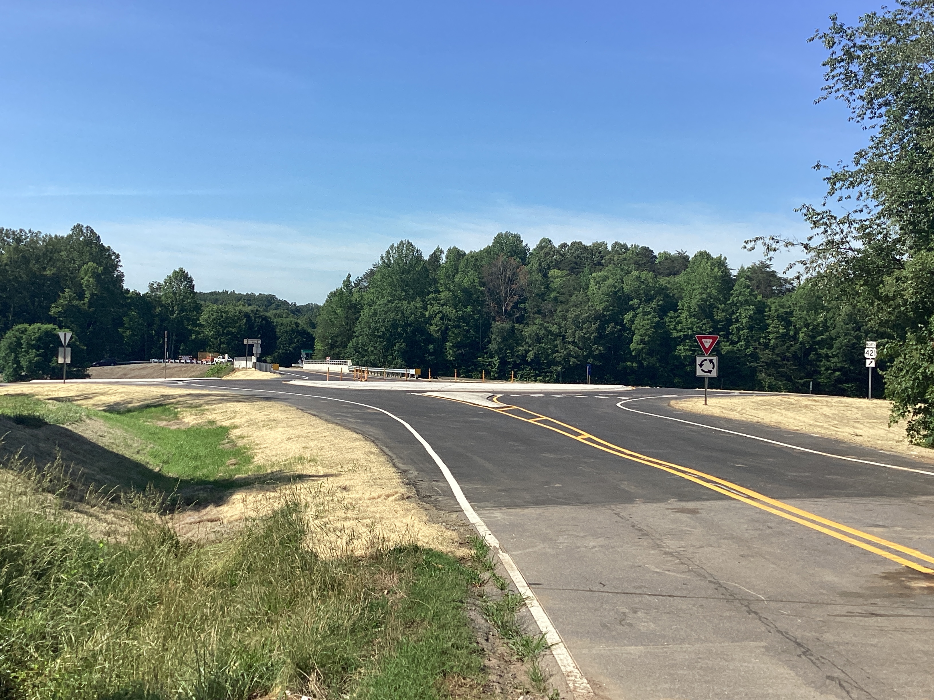 A rural, open road intersection with a roundabout, clear lanes and a yield sign. 