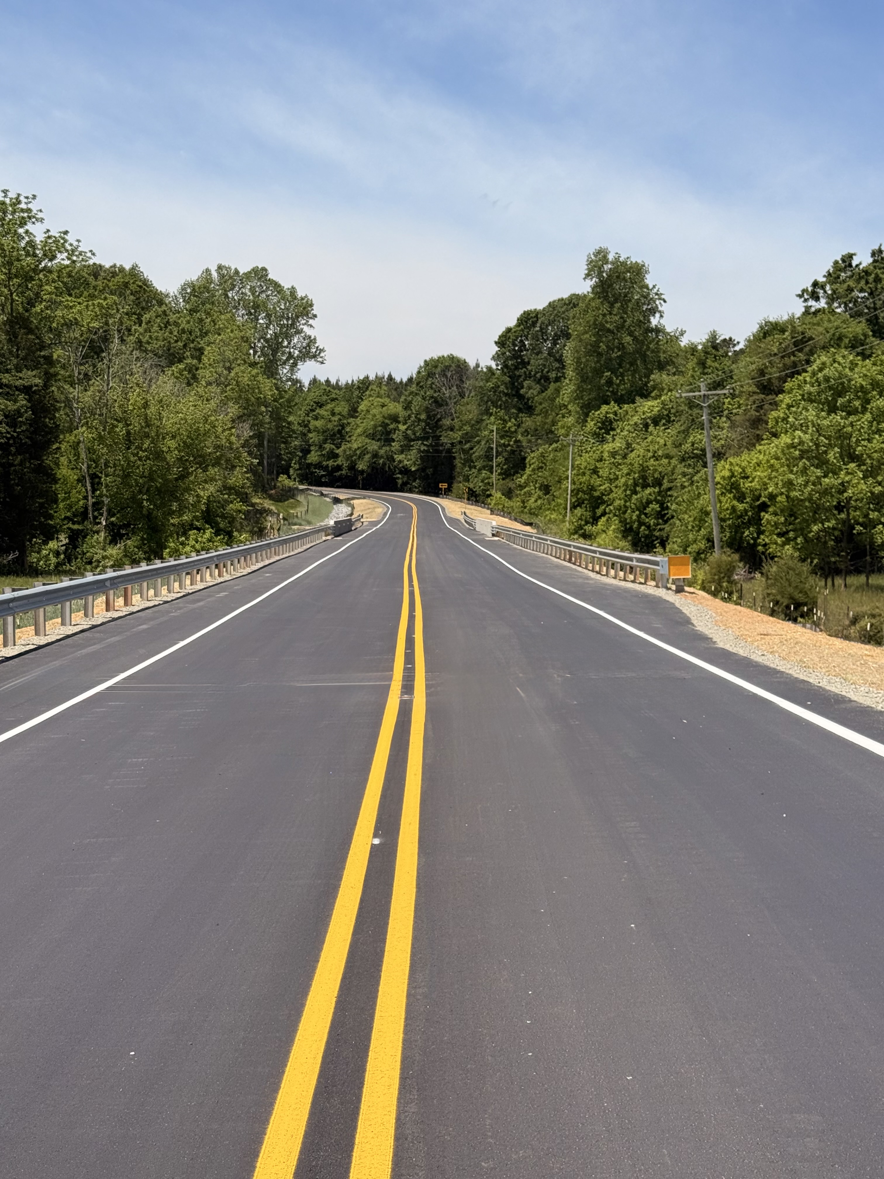 A freshly paved road and bridge is shown under a blue sky. 