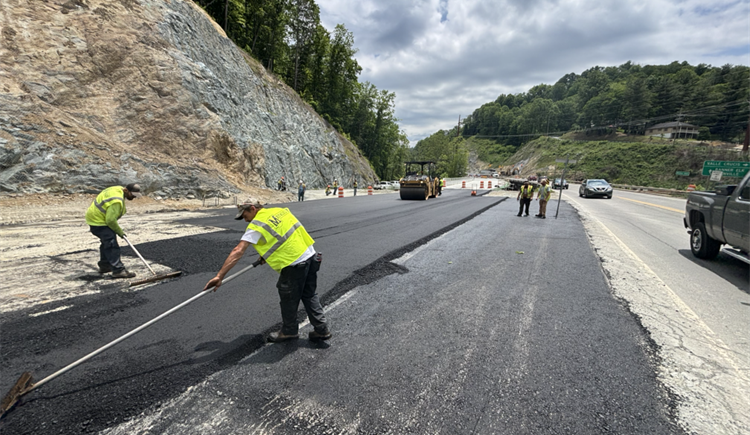 Road construction scene featuring workers in reflective clothing smoothing fresh asphalt on a highway. 