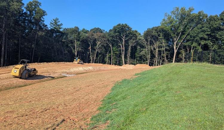 Crews grade a cleared lot under a clear sky. 