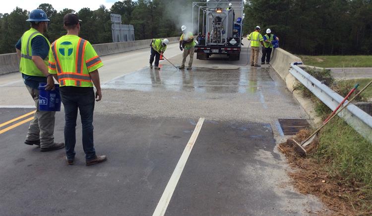 Workers are pouring concrete material over a bridge deck in Robeson County